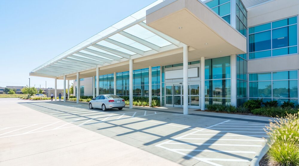 A hospital emergency entrance canopy in daylight with a vehicle waiting on the marked approach lane